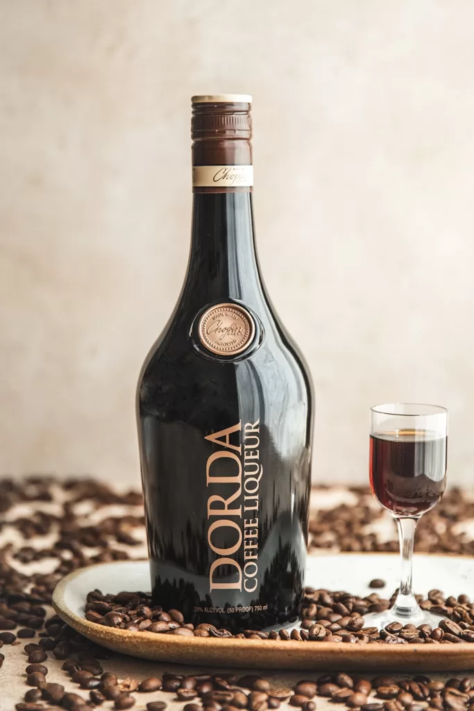 Coffee beans and a glass of coffee liqueur surround Dorda Coffee Bottle.